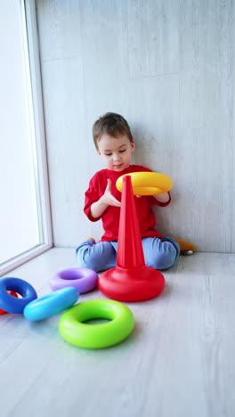 joyful baby boy sitting on the floor plays with pyramid. smiling kid puts a toy detail on his head. vertical video.