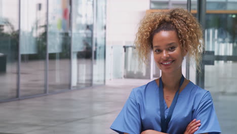 Portrait-Of-Female-Nurse-Wearing-Scrubs-Standing-In-Modern-Hospital-Building