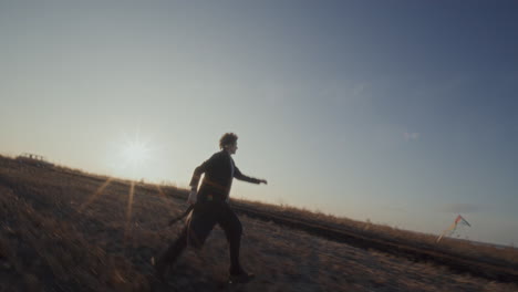 young happy woman flying kite and running across open field at sunset