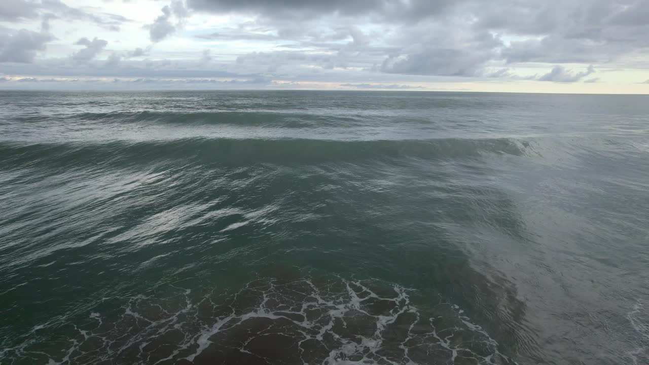 dolly aéreo en las espumosas olas del mar turquesa cerca de la orilla en un día nublado en la playa de dominicalito, costa rica