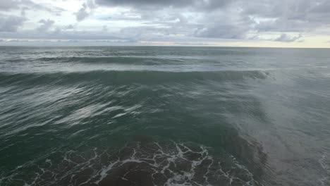 aerial dolly in of foamy turquoise sea waves near the shore on an overcast day in dominicalito beach, costa rica