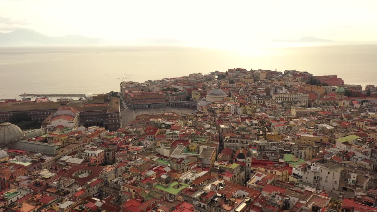 Sorvolo aereo della città storica di Napoli con il centro, il centro antico e il porto con il mare durante la luce dorata del tramonto.