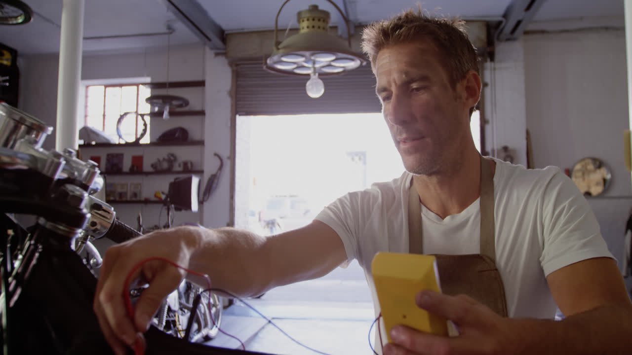 mecánico masculino comprobando la batería de la motocicleta en el garaje de reparación 4k