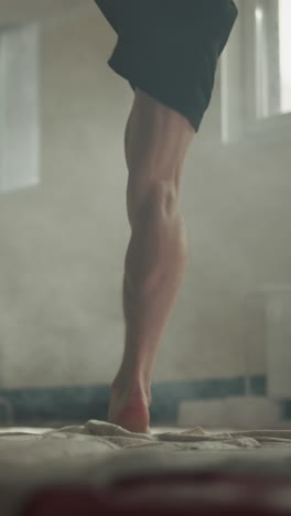 barefoot man hits punching bag by knees in gym closeup. professional sportsman trains leg kicking with heavy equipment in sports club slow motion