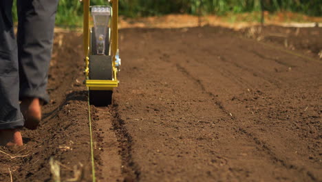 Countryman-using-a-seeder-to-plant-seed-in-the-soil,-cultivating-organic-vegetables