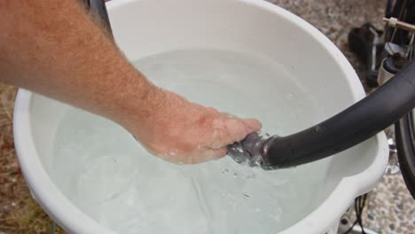 hand pushing punctured bicycle tire in a bucket with water in order to find a leak