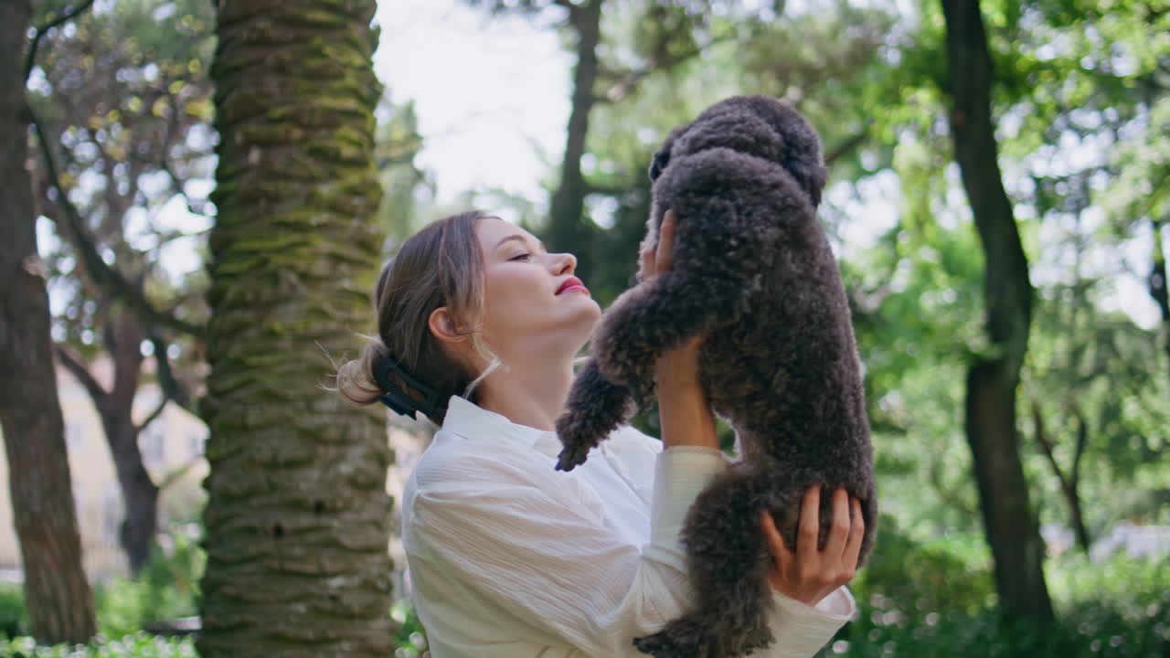Affectionate woman bonding dog on park closeup. Joyful lady holding black poodle