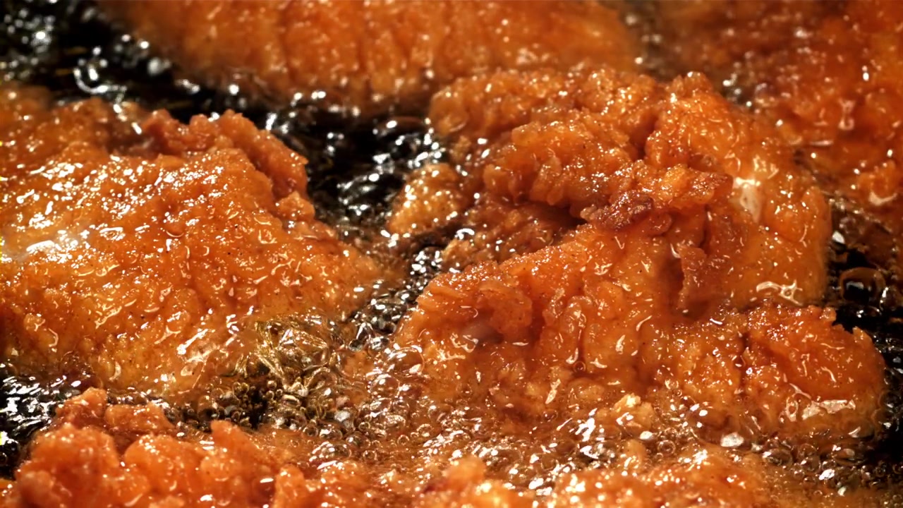 泡立つ油で揚げられるサクサクのフライドチキンのクローズアップ