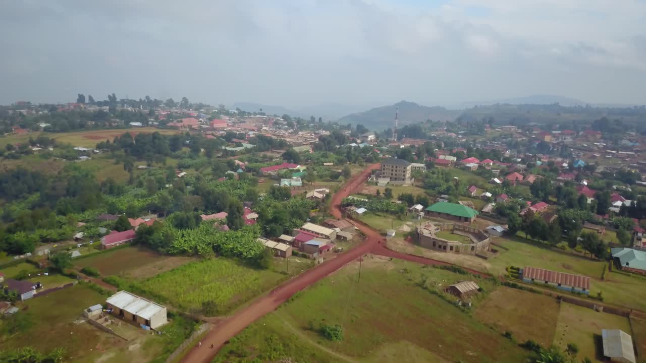 Drone aerial of Kapchorwa in Eastern Uganda showing red dirt roads, dispersed houses, farmlands and lush green slopes of Mount Elgon under soft daylight.