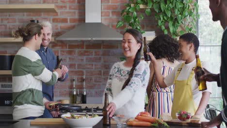 happy group of diverse female and male friends with beer cooking together in kitchen