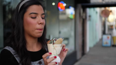 a cute young hispanic woman holding an ice cream cone and smiling with happiness at a dessert shop on a city street