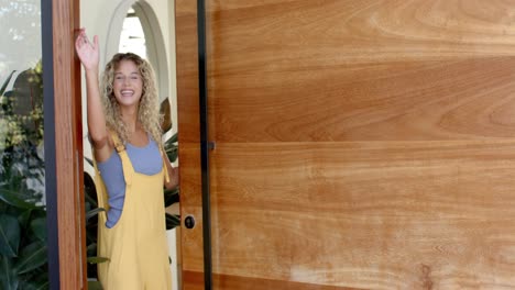 ritratto di una donna caucasica felice a casa che apre la porta d'ingresso, saluta e fa cenno in slow motion