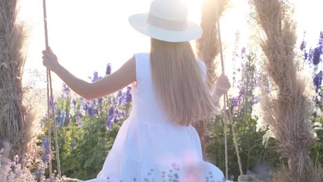 a blonde in white clothes rides on a swing in the middle of wildflowers a blonde in white clothes rides on a swing in the middle of wildflowers photo session in the field against the background of the suns rays happiness from enjoying nature