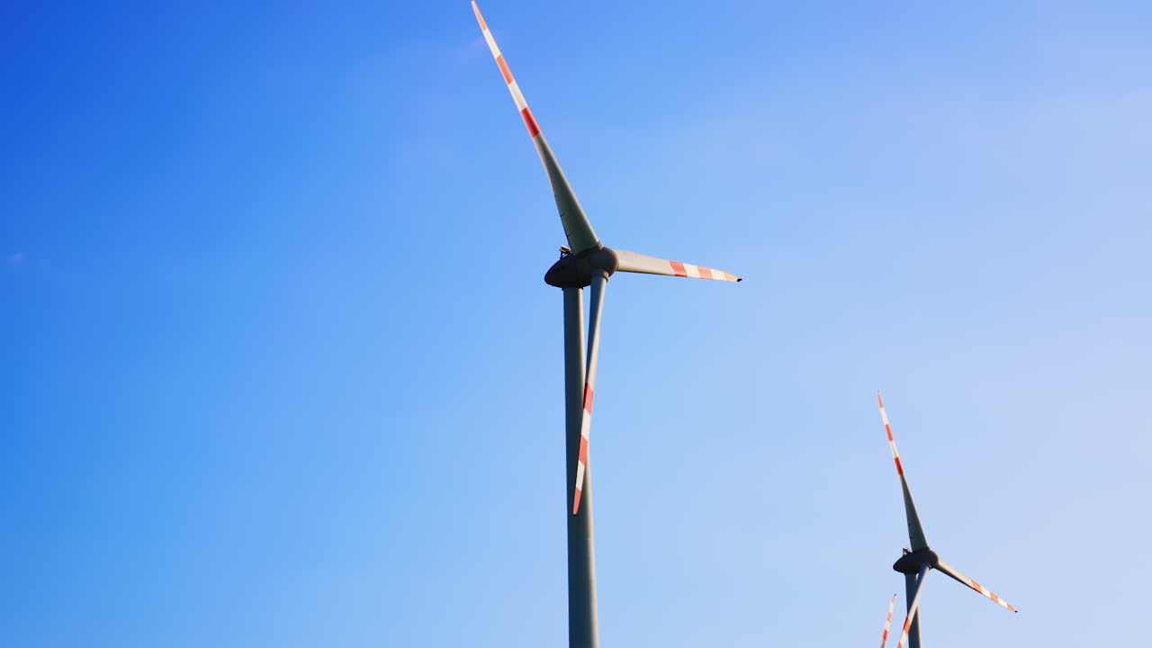 Wind turbines spinning in clear blue sky. Two wind turbines rotate gracefully beneath a vibrant blue sky, showcasing renewable energy in action at midday