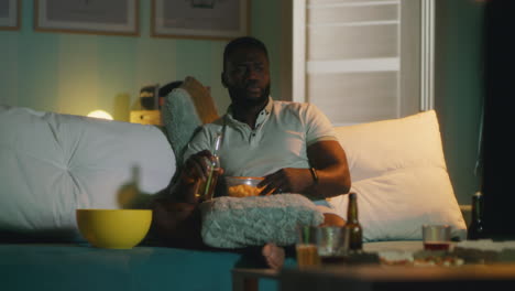 man watching tv at home with beer and popcorn