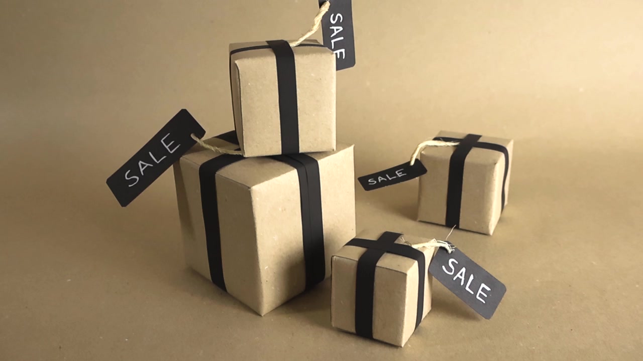 Pile of gift boxes in kraft paper with black ribbons and sale tags orbiting on a light brown background. Special offer concept for Black Friday, Cyber Monday, Christmas or holidays