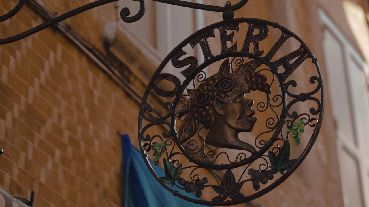 Enseigne de rue en métal avec une silhouette de Bacchus et des détails de grappes de raisin, suspendue à l'extérieur d'une authentique osteria italienne