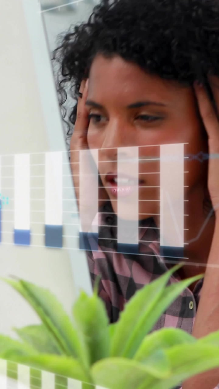 Vídeo vertical: Mulher analista analisando dados financeiros na tela enquanto gráficos atualizam, planta em primeiro plano.