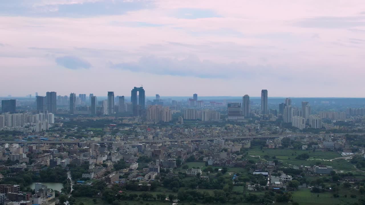 Aerial drone shot of skyscrapers on the horizon, small buildings in the foreground set against pink monsoon clouds showing the stages of development in Delhi, Mumbai, Bangalore, Hyderabad