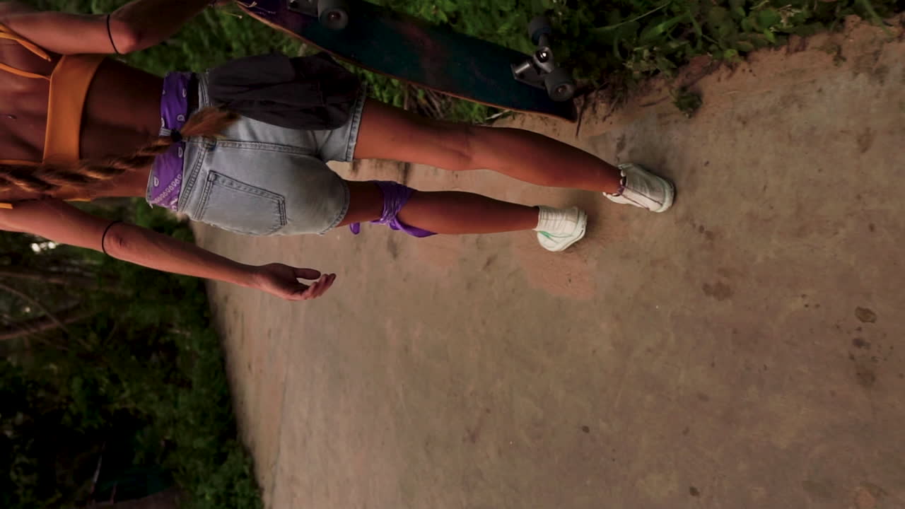 Sporingsoptagelse bagfra af en blond pige, der går og holder et skateboard.