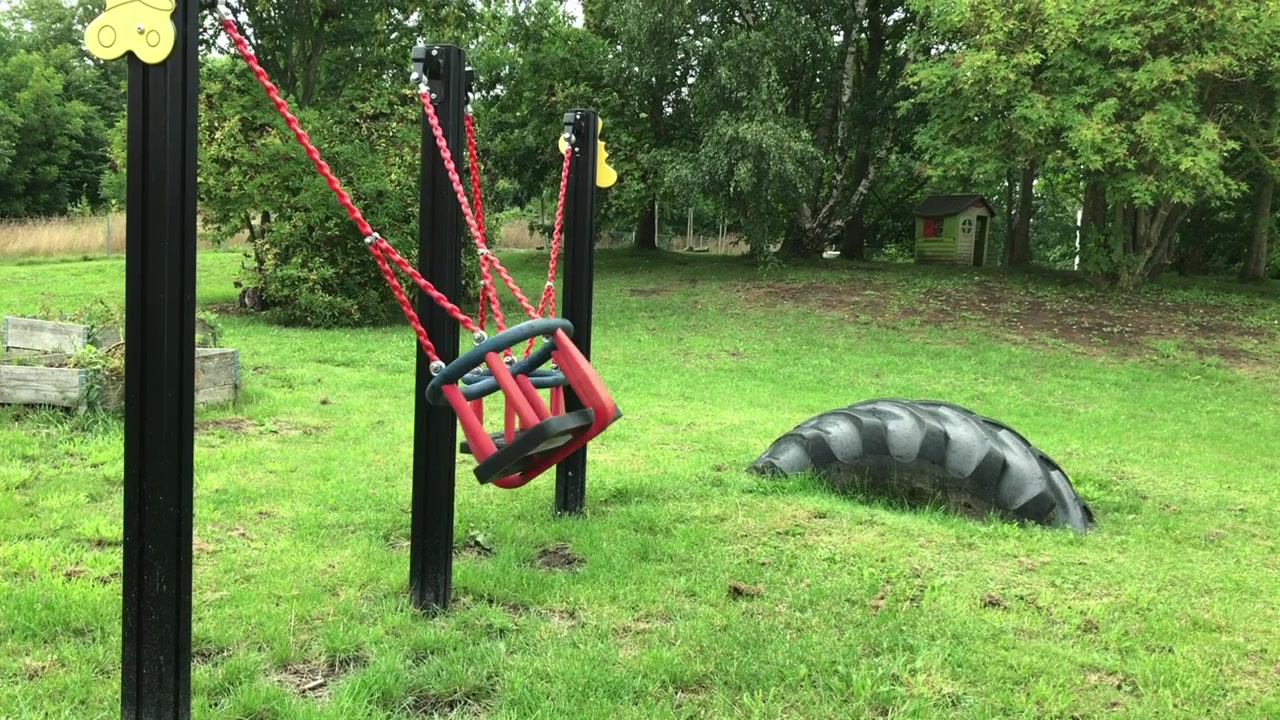 Vídeo de um balanço vermelho solitário balançando para frente e para trás em um parquinho vazio em Eslöv, Suécia