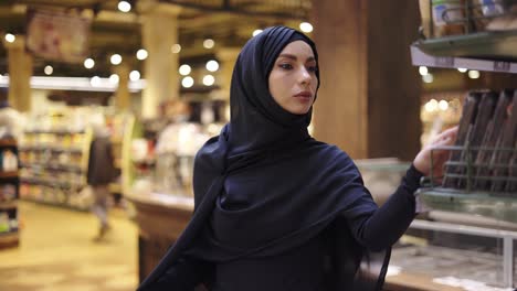 woman in hijab takes pile of products from the shelf in the supermarket