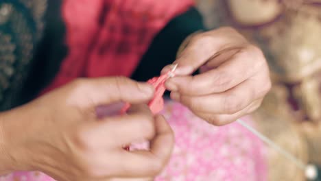 primer plano de las manos de una anciana tejiendo con agujas artesanales y lana roja