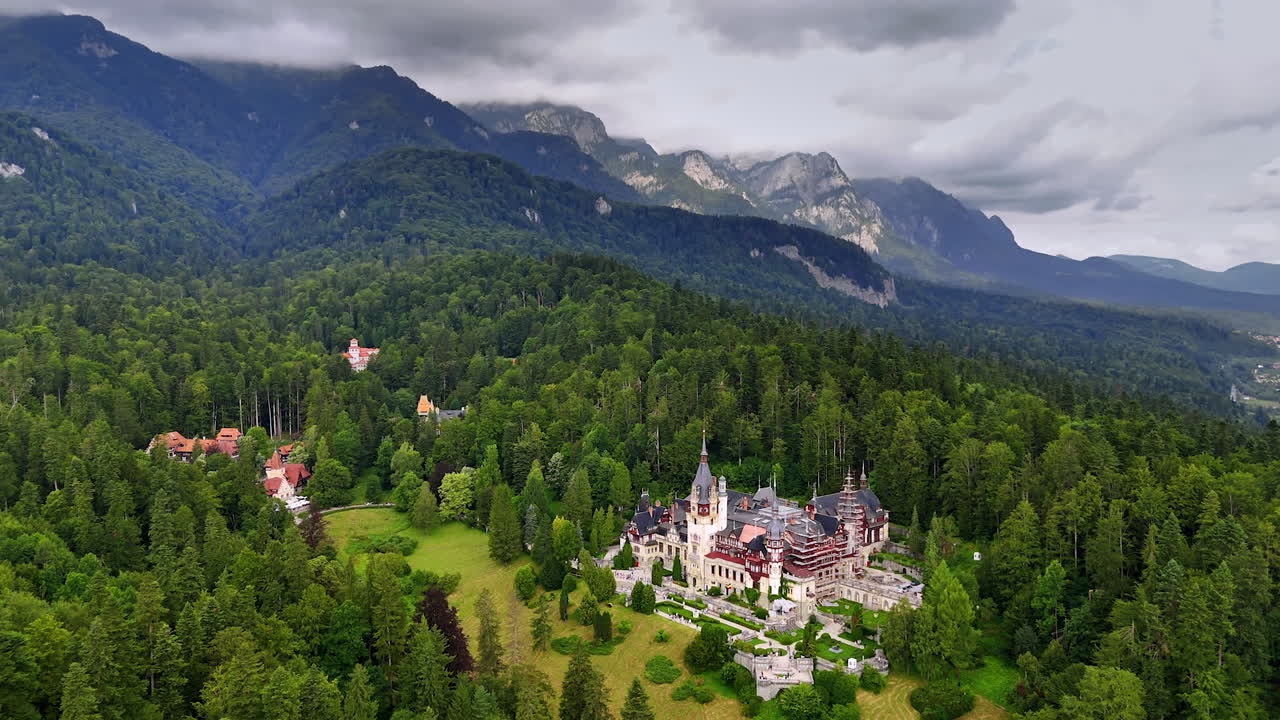 Spectacular Carpathian Mountains covered with pine tree woods. Peles Castle, Prahova County, Romania is in the meadow. Grey clouds cover the sky above