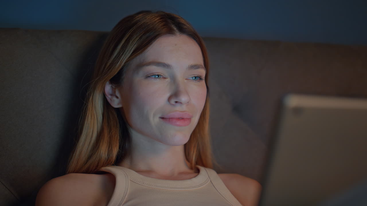 Sleepy girl reading ebook lying dark bedroom close up. Woman looking on tablet