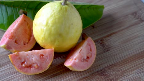 fruta de guayaba amarilla y rosa fresca entera y en rodajas sobre fondo de madera, toma panorámica de primer plano