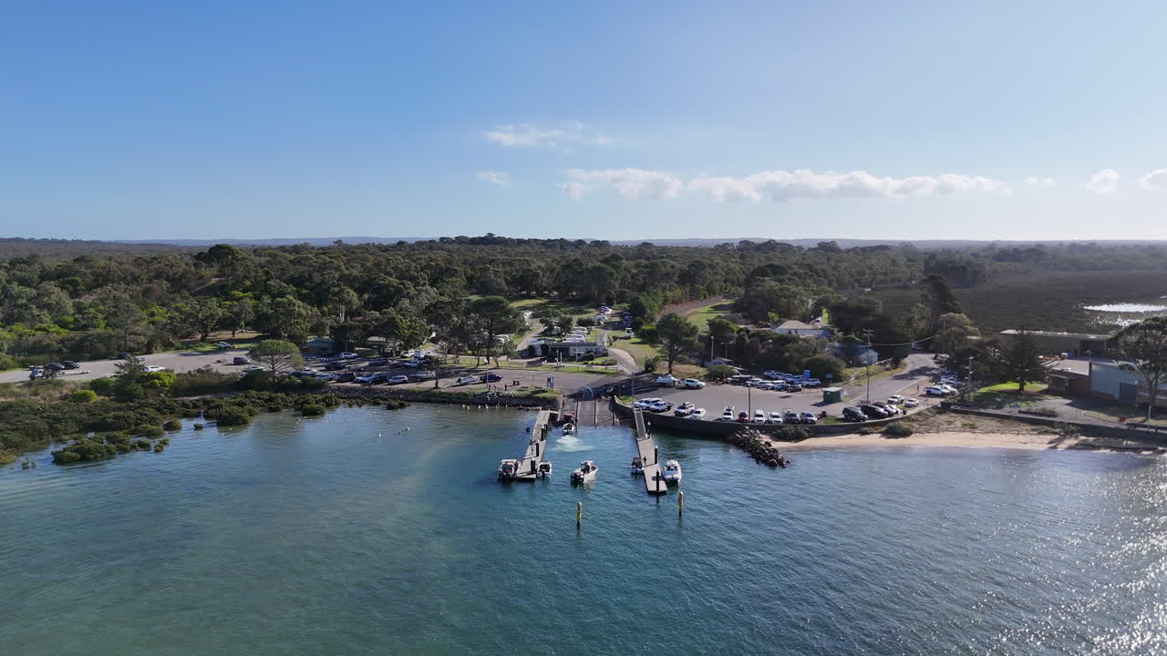Amidst a picturesque setting, boats maneuver gently for their places at the mooring while framed by lush greenery and soft sunlight. The lively atmosphere captures the essence of waterfront activity.