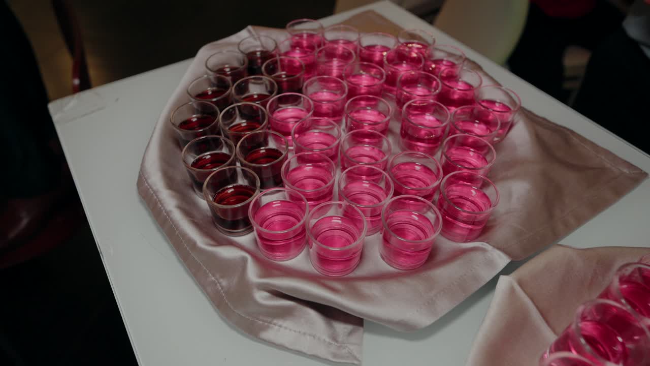 Array of pink and red shots arranged on a satin cloth, prepared for an event or celebration