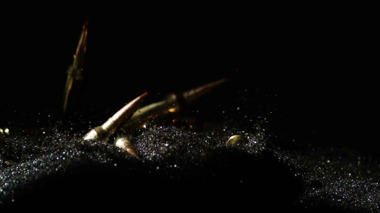 Slow motion shot of golden 6mm ARC bullets falling on black sand,close up