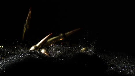 slow motion shot of golden 6mm arc bullets falling on black sand,close up