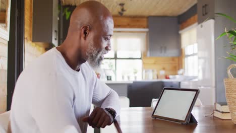 Glücklicher-älterer-Afroamerikanischer-Mann,-Der-Am-Tisch-Sitzt-Und-Ein-Tablet-Mit-Kopierraum-Benutzt,-Zeitlupe