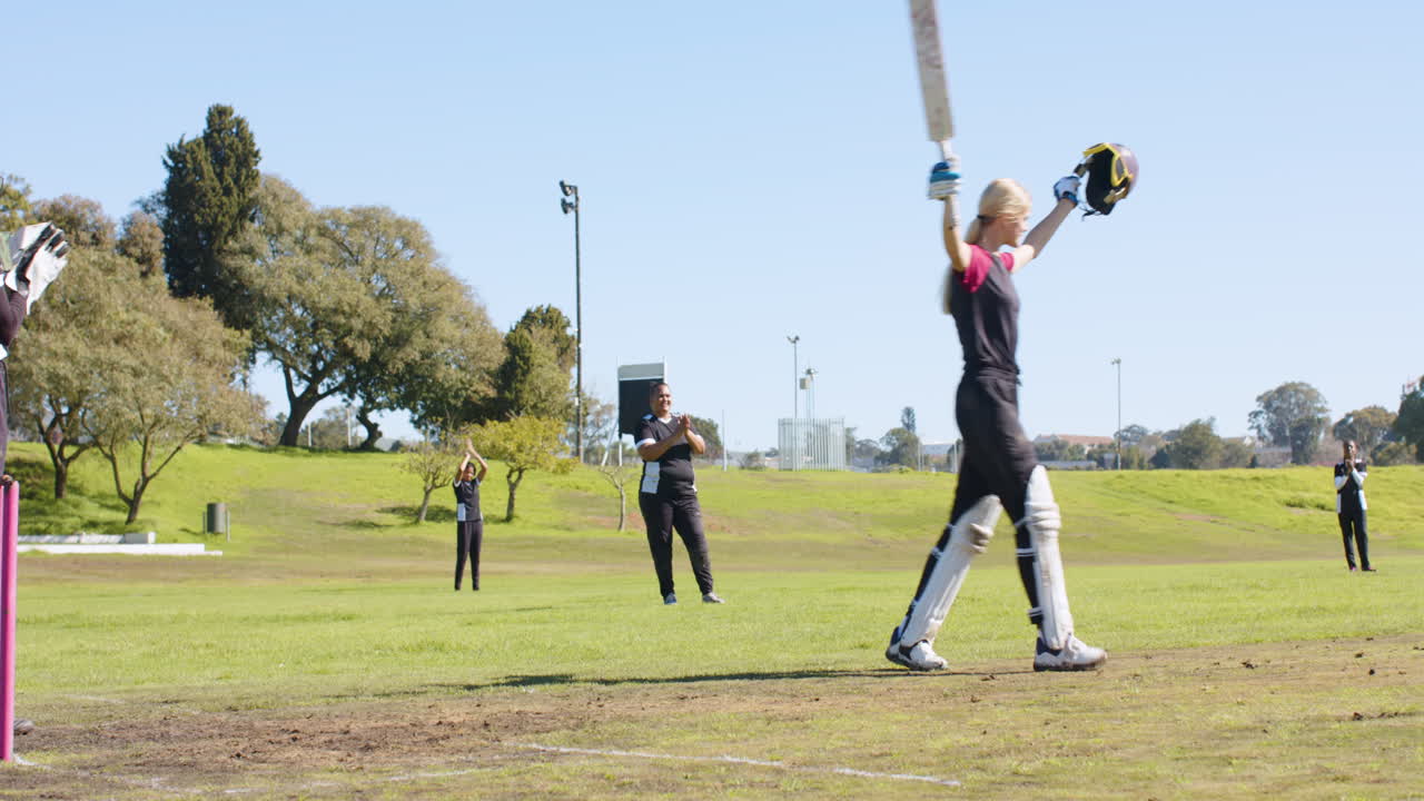 Celebrating victory, female cricketer raising bat and helmet on cricket field
