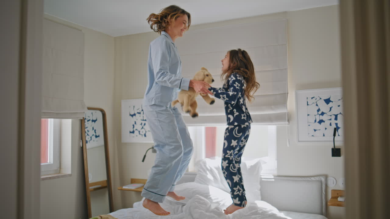 Carefree family jumping bed in house. Overjoyed mom kid having fun together