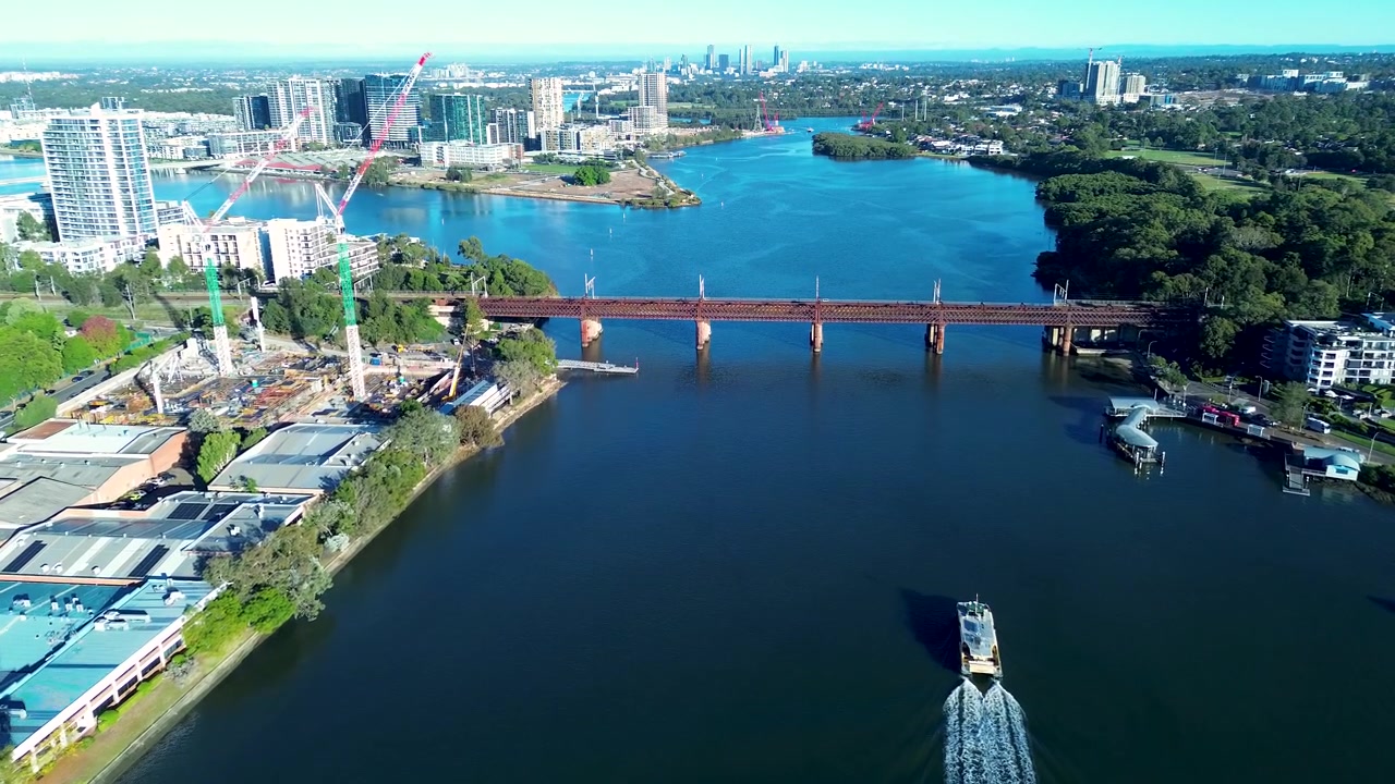 Drone-ilmakuva työmatkalautasta risteilemässä Parramatta-joen vesistöissä, rautatiesillan ja urbaanien ranta-rakennusten ympäröimänä Meadowbankissa, Sydneyssä, Australiassa, esitellen alueen liikenneinfrastruktuuria.