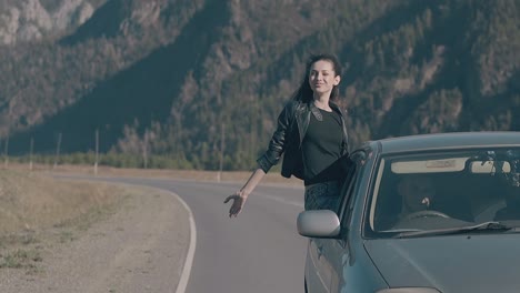 elated lady sits on blue speeding car and raises hand to sky