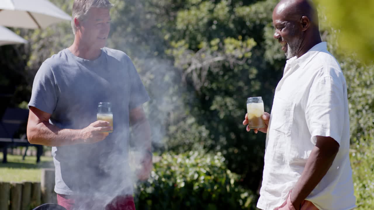 Two diverse senior men enjoying drinks and conversation at in garden barbecue gathering