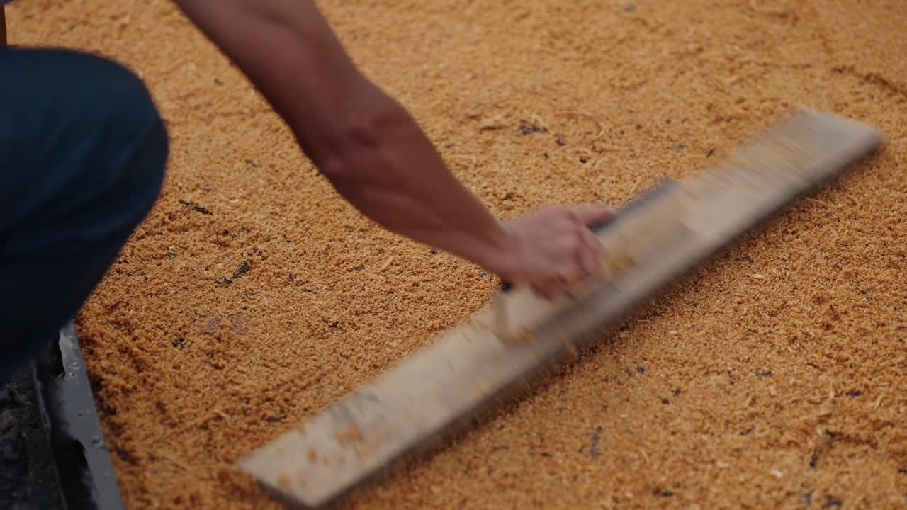 Close-up of a person smoothing sawdust to create a traditional Semana Santa alfombra on cobblestone streets.
