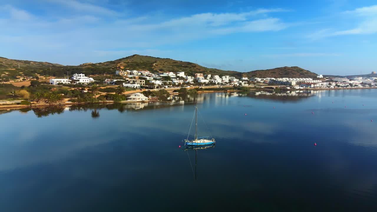 Reflection of sailing boat floating on water with mountain village in the background