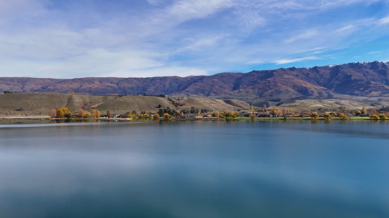 Drone captures serene Lake Dunstan with surrounding mountains under clear blue skies, showcasing natural beauty and tranquility