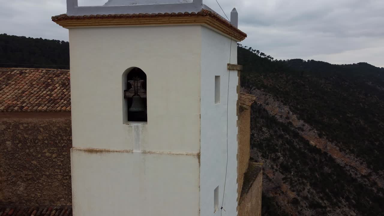 Ripresa aerea 4K con drone di un tradizionale campanile di chiesa bianco che si affaccia sul canyon del fiume Júcar. Vista panoramica di acque turchesi e lussureggianti pinete in Castilla-La Mancha, Spagna.