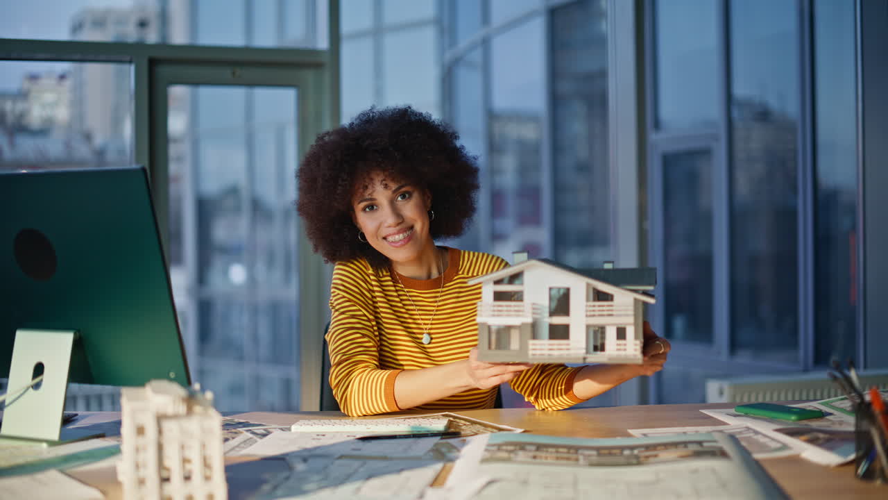 Ingegnere professionista che mostra il modello di una casa alla fotocamera in ufficio. Donna sorridente
