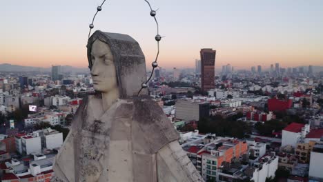 dramatic medium drone shot of massive jesus status towering over mexico city at sunset, featuring parroquia del purism corazon de maria and buildings in the back