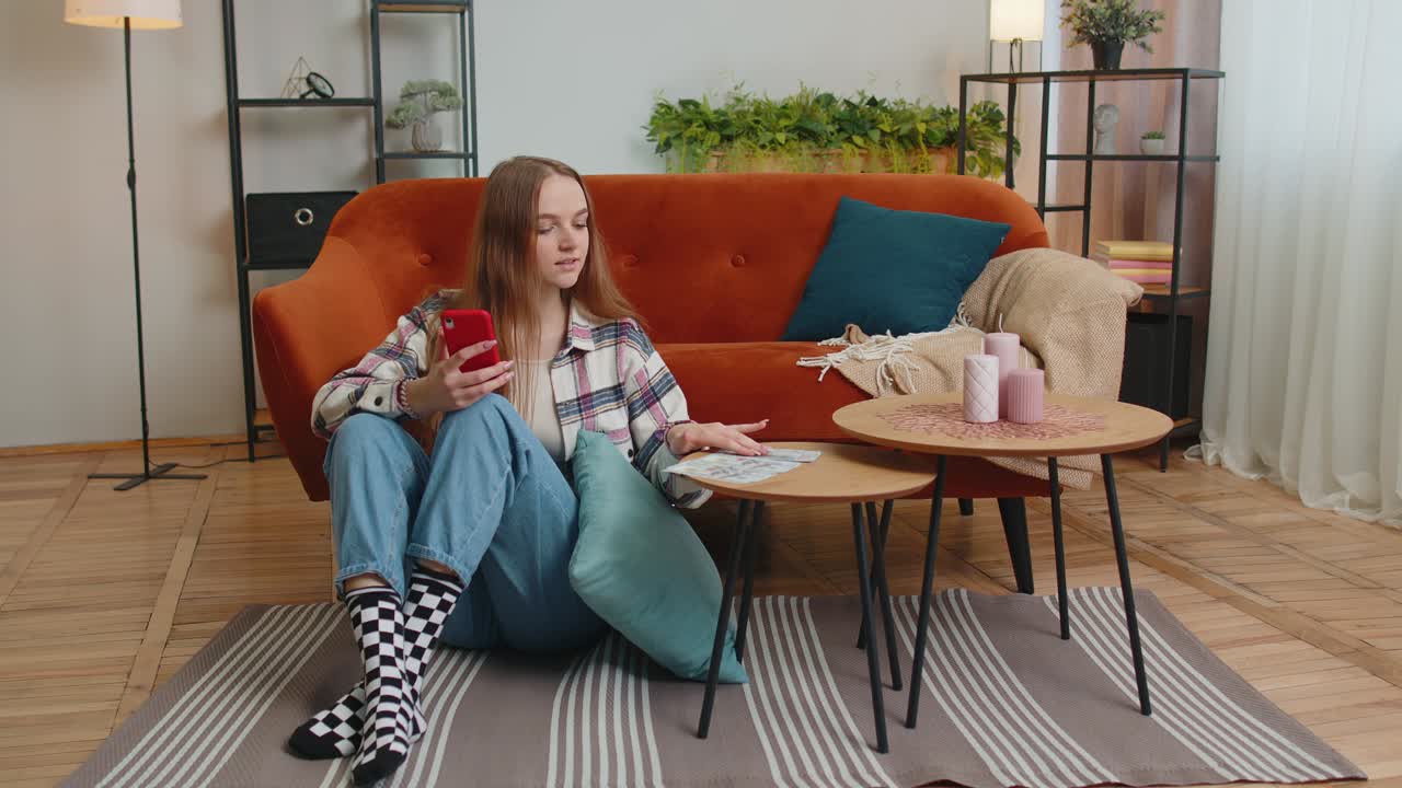sonriente joven feliz contando dinero en efectivo y usar teléfono móvil calcular facturas domésticas en casa