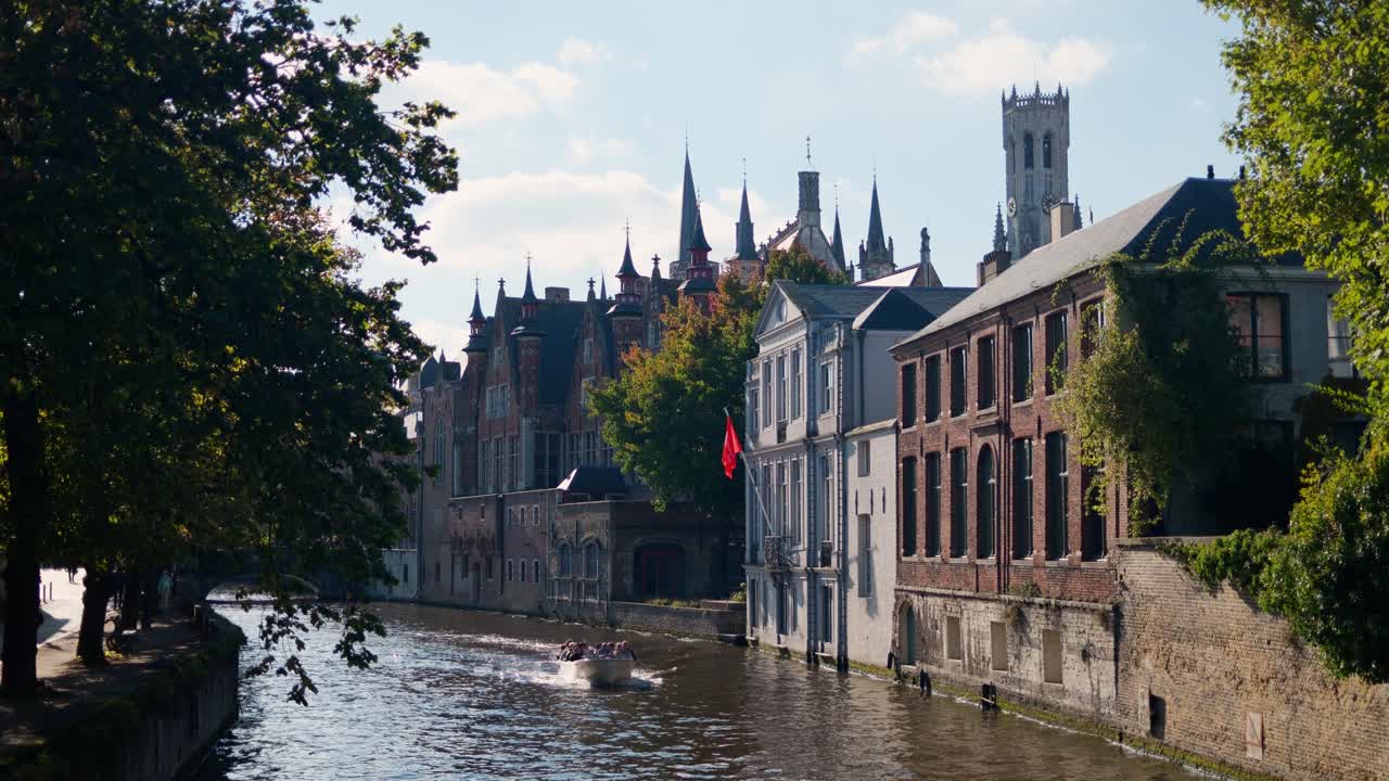 Tourist boat gliding through Bruges canal surrounded by historic buildings on a sunny day