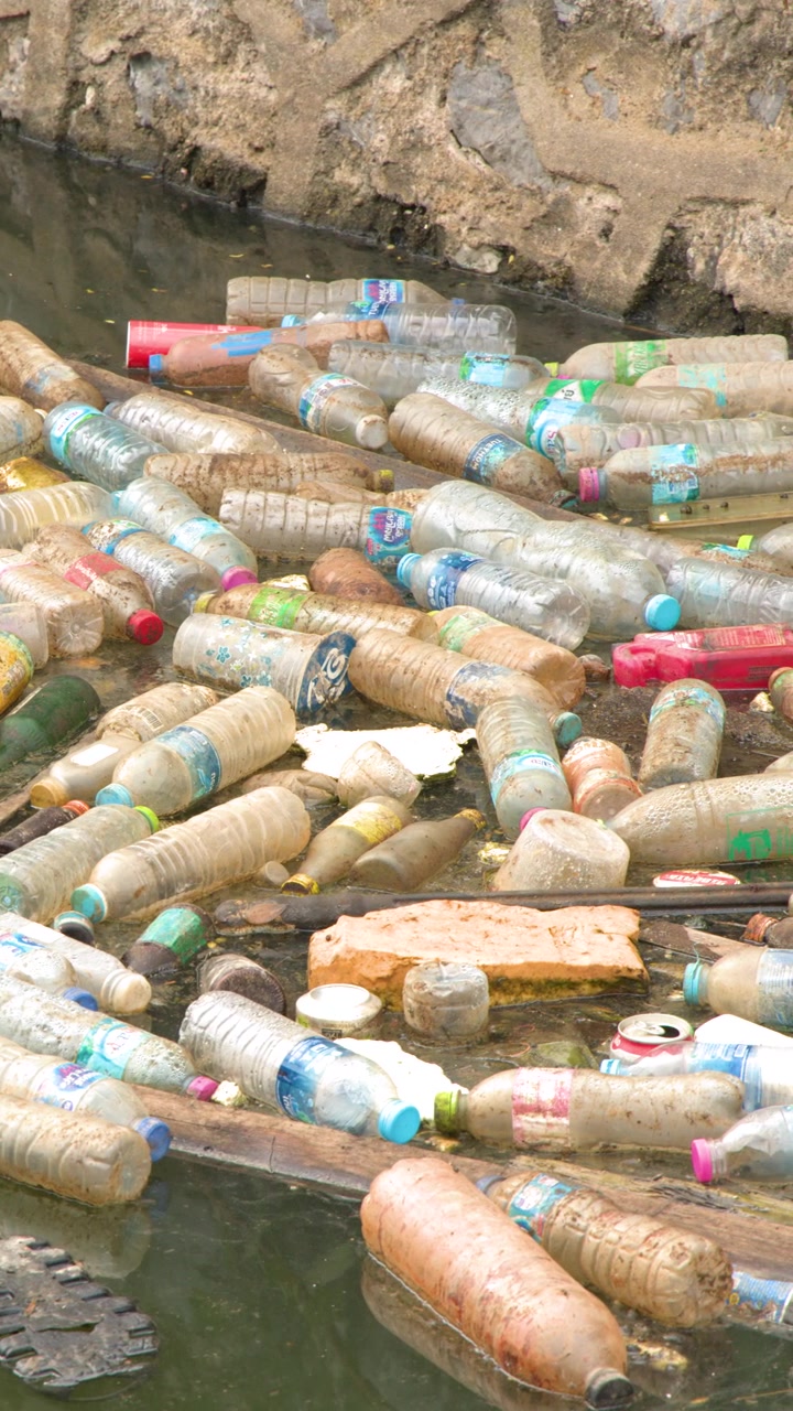 Inquadratura statica dall'alto di bottiglie di plastica scartate e rifiuti che galleggiano nell'acqua sporca di un fiume.