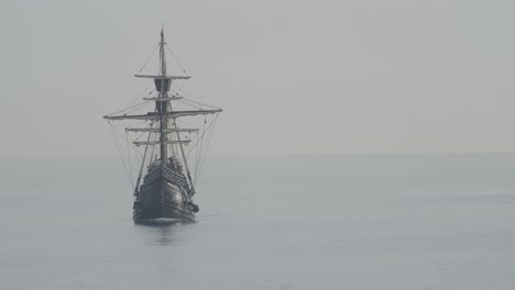 ferdinand magellan nao victoria carrack boat replica with spanish flag sails in the mediterranean at sunrise in calm sea front shot turning in slow motion 60fps